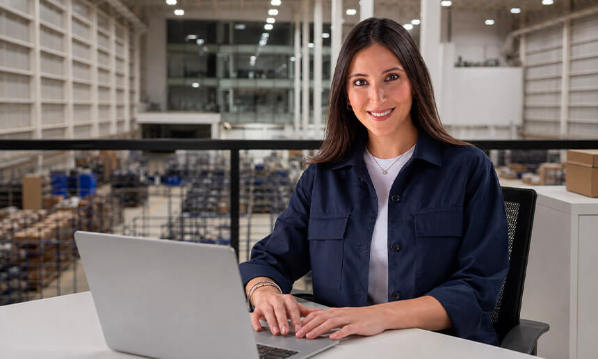Woman wearing a navy blue corporate jacket while working on a laptop inside a warehouse