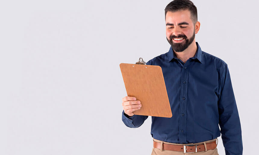 Bearded man wearing a navy blue shirt, smiling while reviewing a clipboard
